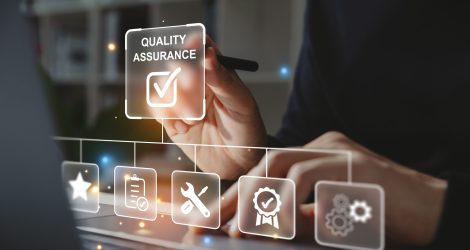 Hand of businessman holding a pen pointing to Quality Assurance icon for service guarantee on laptop screen,  Standards control and certification concept.